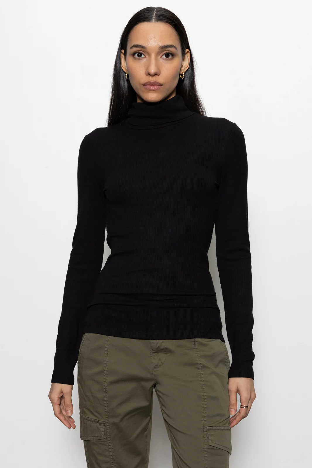 Person wearing a black turtleneck and green pants on a white background