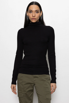 Person wearing a black turtleneck and green pants on a white background