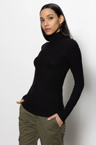 Woman wearing a black turtleneck and green pants against a white background