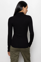 Person wearing a black long-sleeve top and green pants on a white background