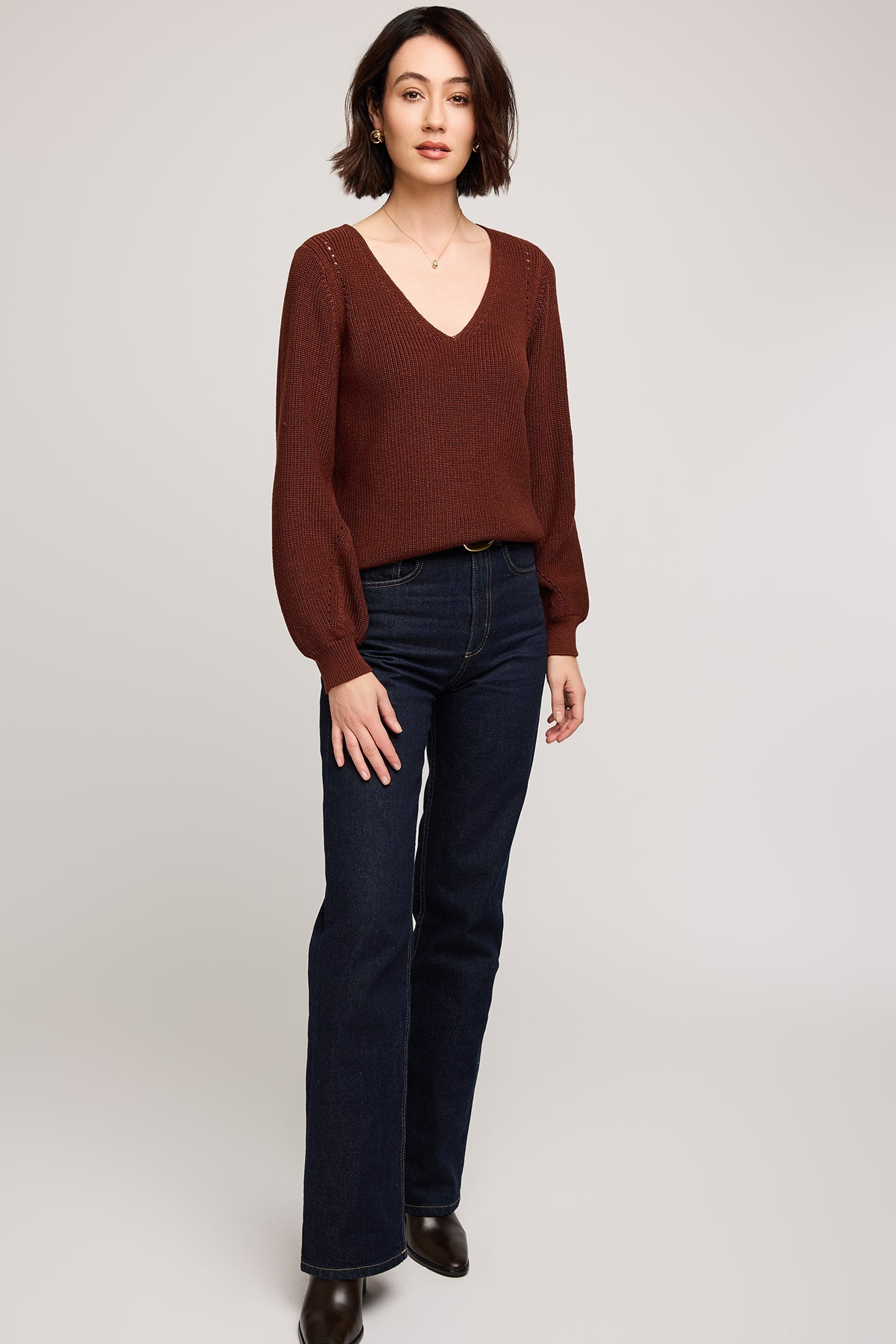 Woman wearing a brown sweater and dark jeans on a plain background