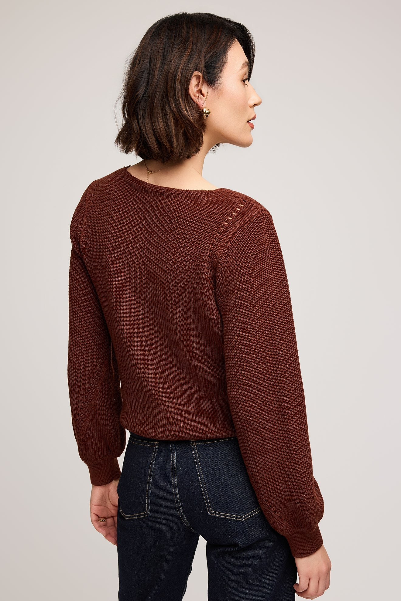 Woman wearing a brown sweater and dark jeans on a plain background