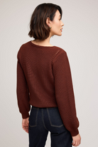 Woman wearing a brown sweater and dark jeans on a plain background
