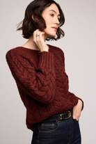 Woman wearing a maroon cable knit sweater against a plain background