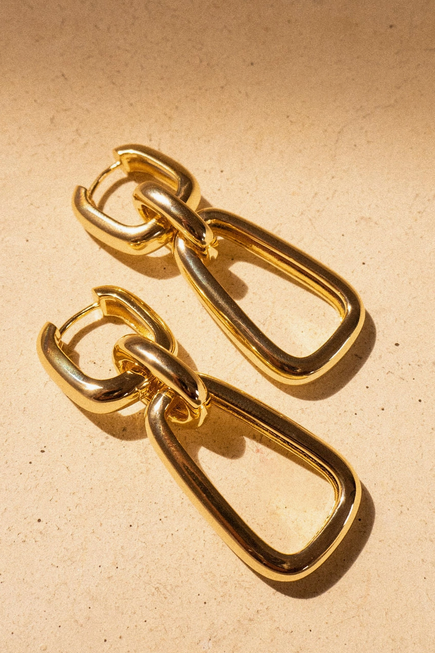 Pair of gold chain-style earrings on a beige background
