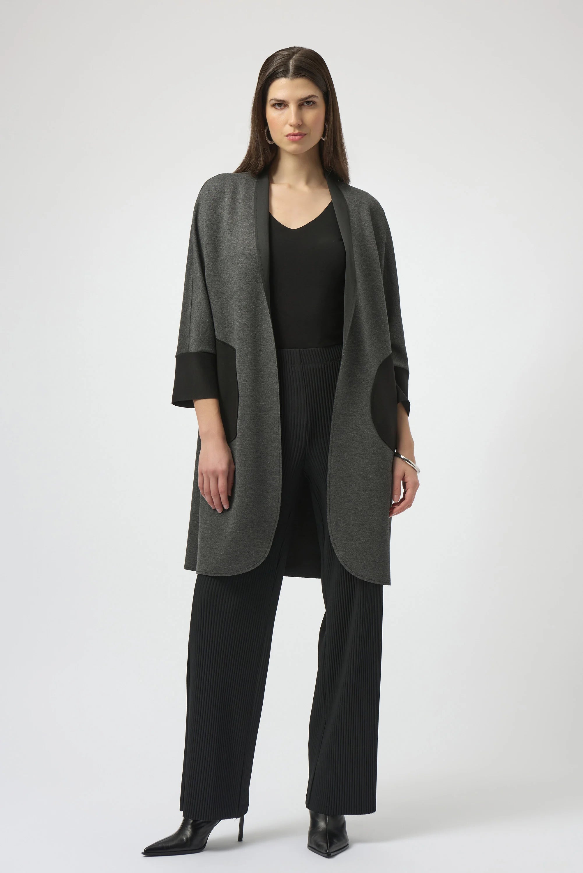 Woman wearing a long gray coat over a black outfit on a white background