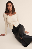 Woman wearing a white top and black skirt sitting on a white background