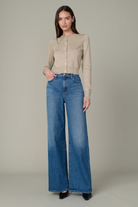 Woman wearing a beige blouse and blue jeans against a plain background