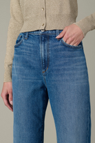Person wearing blue jeans and a beige cardigan on a neutral background