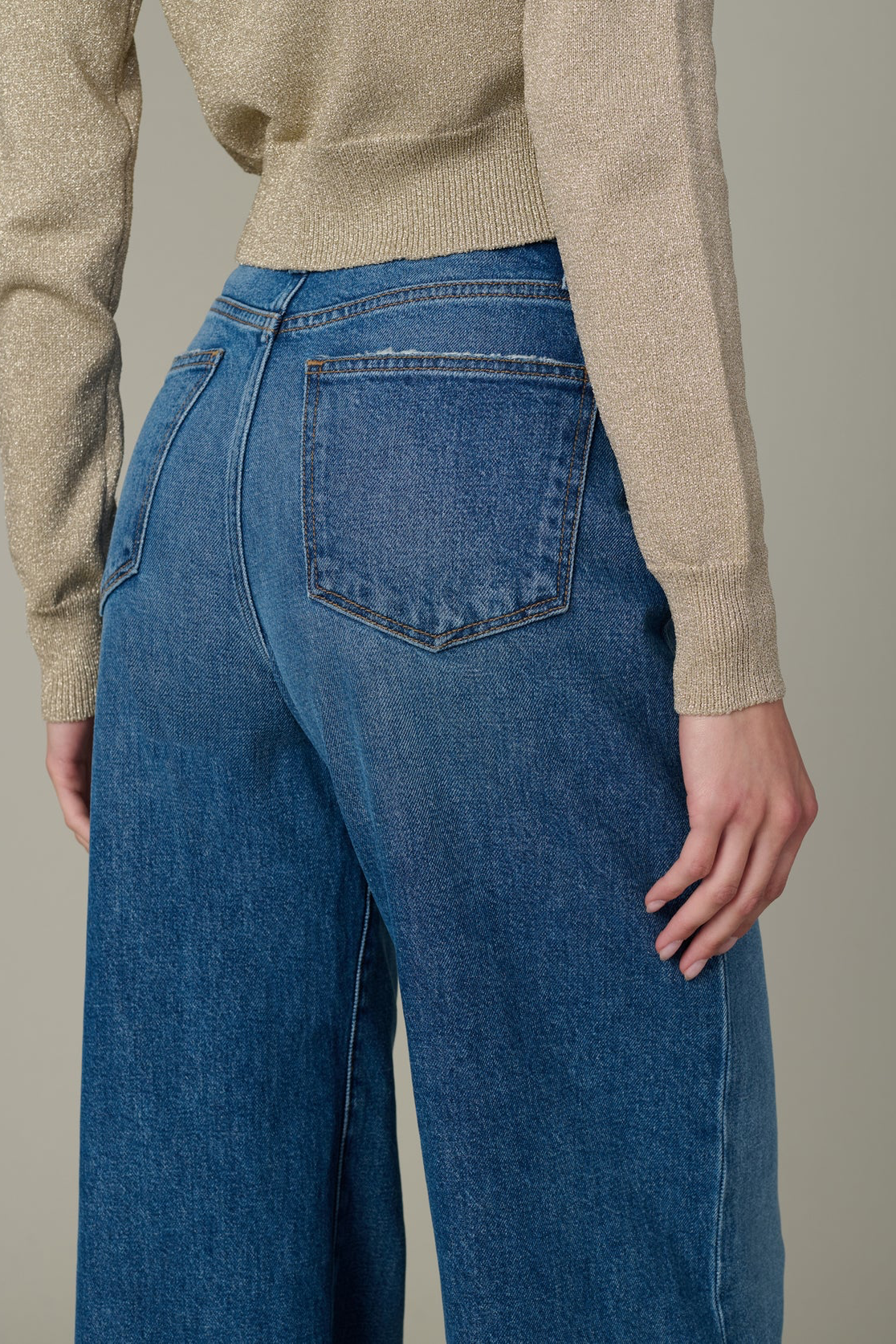 Person wearing blue jeans and a beige sweater against a neutral background