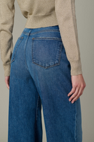 Person wearing blue jeans and a beige sweater against a neutral background