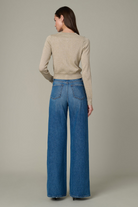 Woman wearing a beige sweater and blue jeans against a neutral background