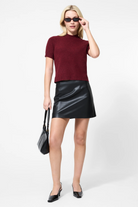 Woman wearing a burgundy top and black leather skirt on a white background