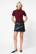 Woman wearing a burgundy top and black leather skirt on a white background