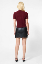 Person wearing a burgundy top and black leather skirt on a white background