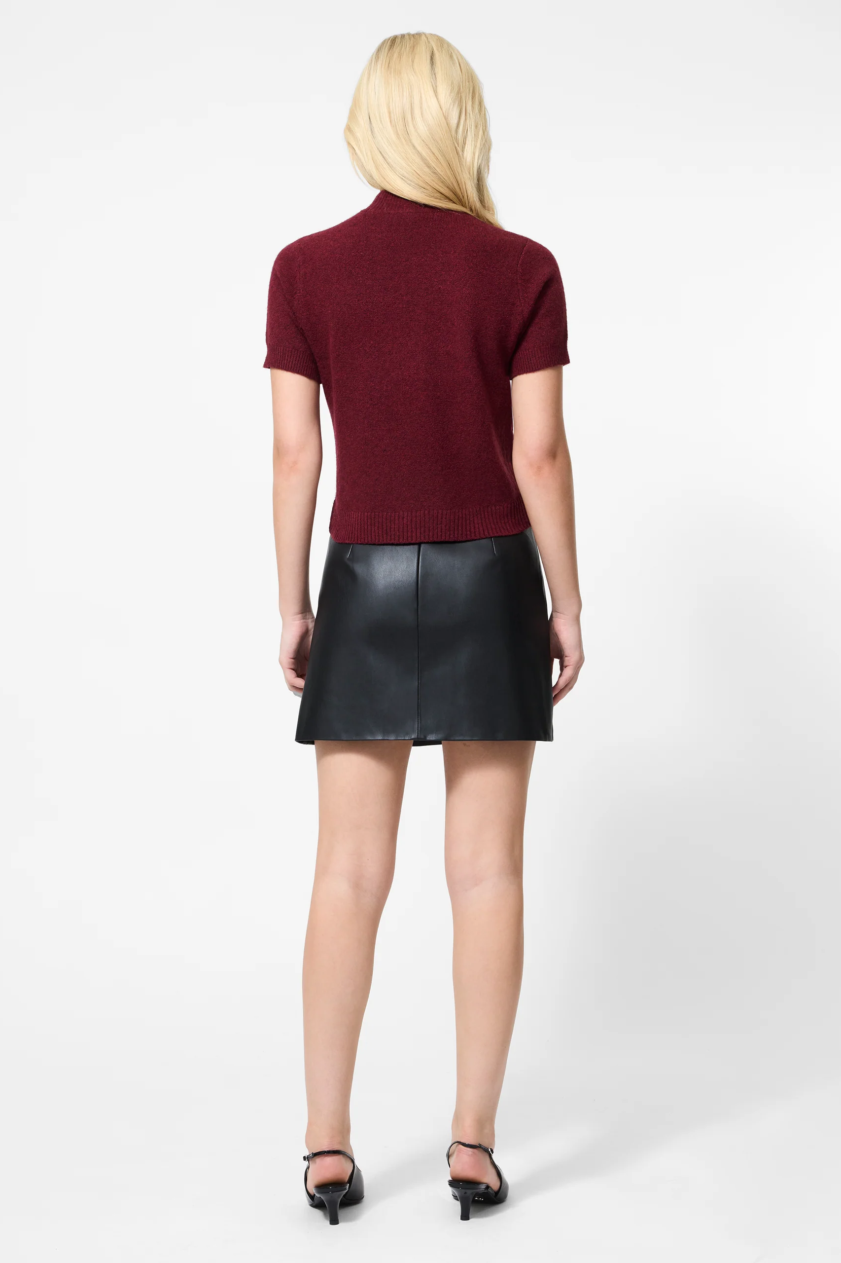 Person wearing a burgundy top and black leather skirt on a white background