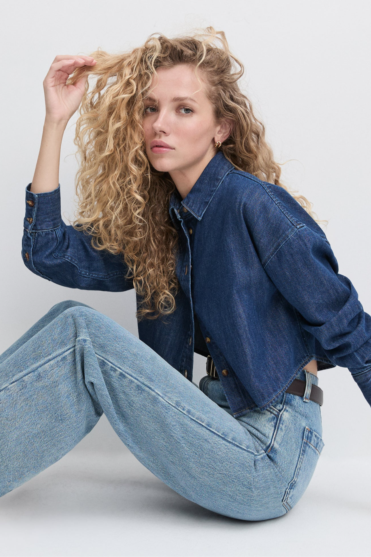 Woman wearing a denim jacket and jeans sitting on a white background