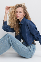 Woman wearing a denim jacket and jeans sitting on a white background
