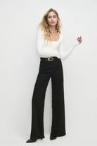 Woman wearing a white long-sleeve top and black wide-leg pants on a light gray background