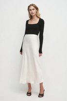 Woman wearing a black long-sleeve top and white skirt on a white background
