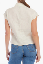 Person wearing a beige sleeveless shirt and blue jeans on a white background