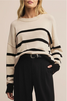 Person wearing a cream sweater with black stripes and black pants on a beige background