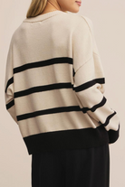 Beige sweater with black stripes worn by a person on a beige background