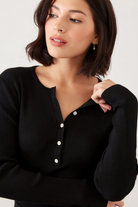 Woman wearing a black ribbed sweater with white buttons on a plain background