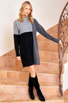 Woman wearing a gray and black dress with black boots standing on a staircase.