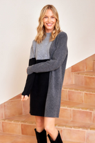 Woman wearing a gray cardigan over a black dress on a beige staircase.