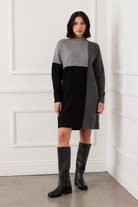 Woman wearing a black and gray dress with knee-high boots against a white wall.