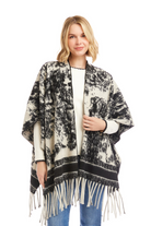 Woman wearing a black and white patterned poncho with fringe on a white background