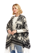 Woman wearing a black and white patterned poncho with fringe on a white background