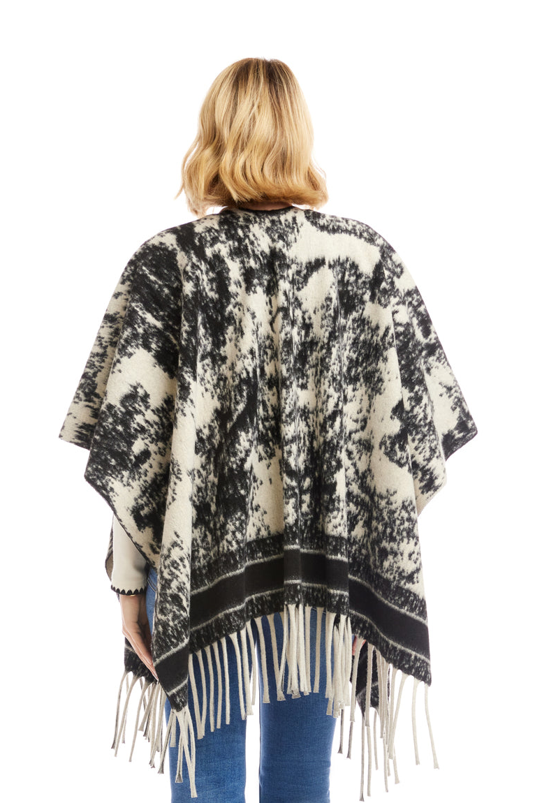 Woman wearing a black and white patterned poncho with fringe on a white background