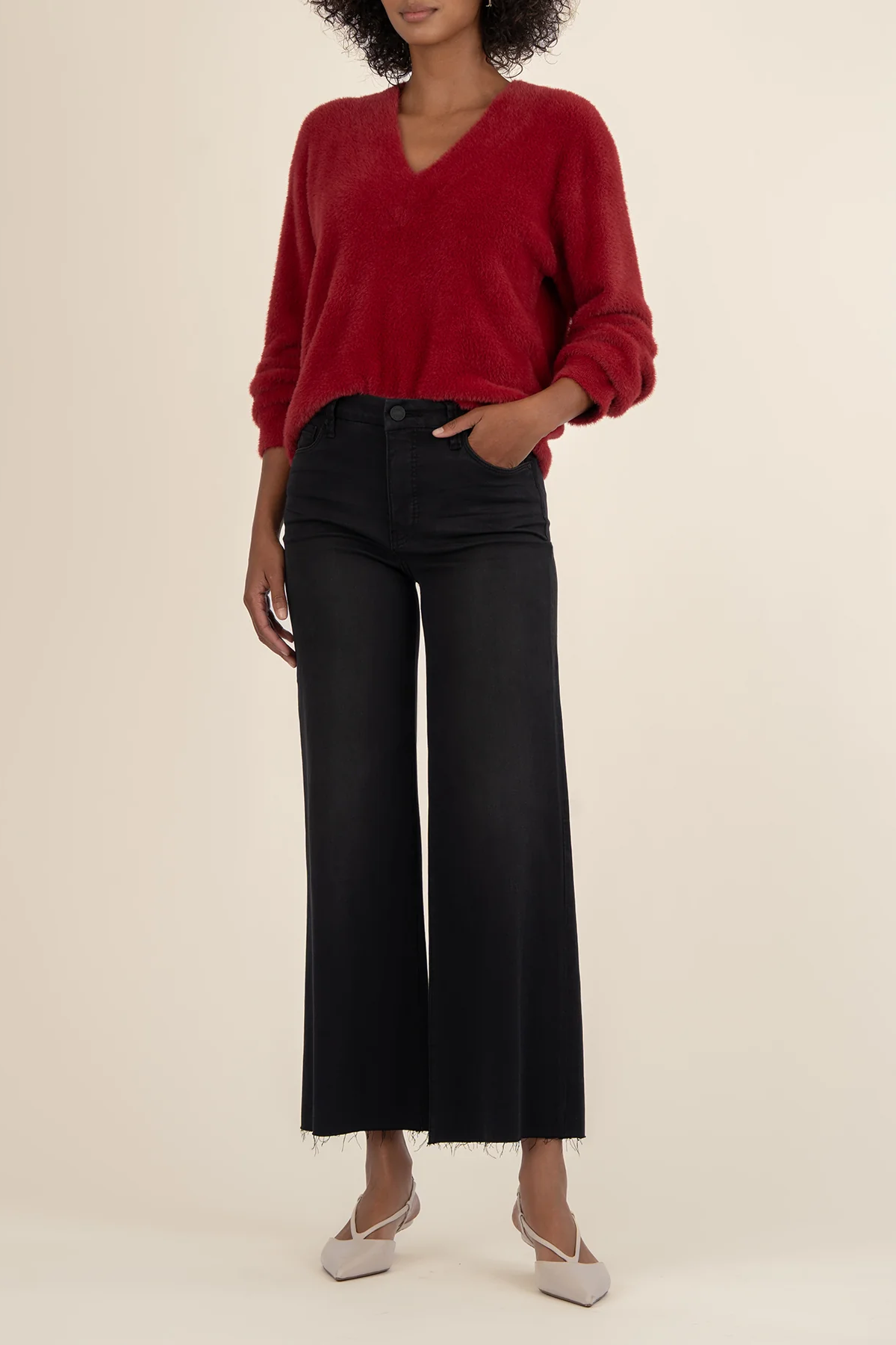Person wearing a red sweater and black pants on a beige background