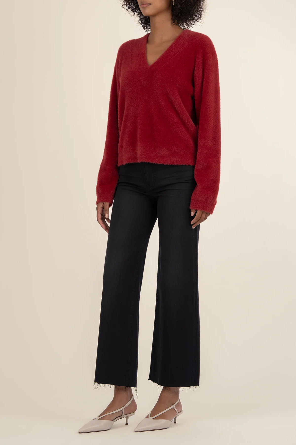Person wearing a red sweater and black pants on a beige background