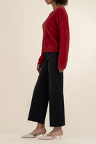 Person wearing a red sweater and black pants on a beige background
