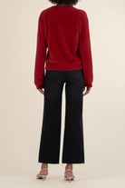 Person wearing a red sweater and black pants on a beige background