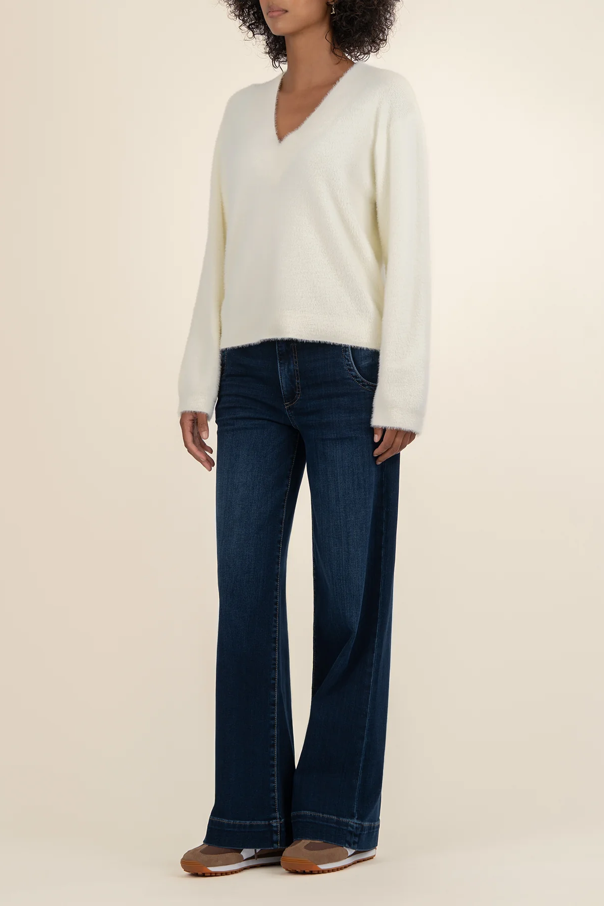 Person wearing a white sweater and dark blue jeans on a beige background