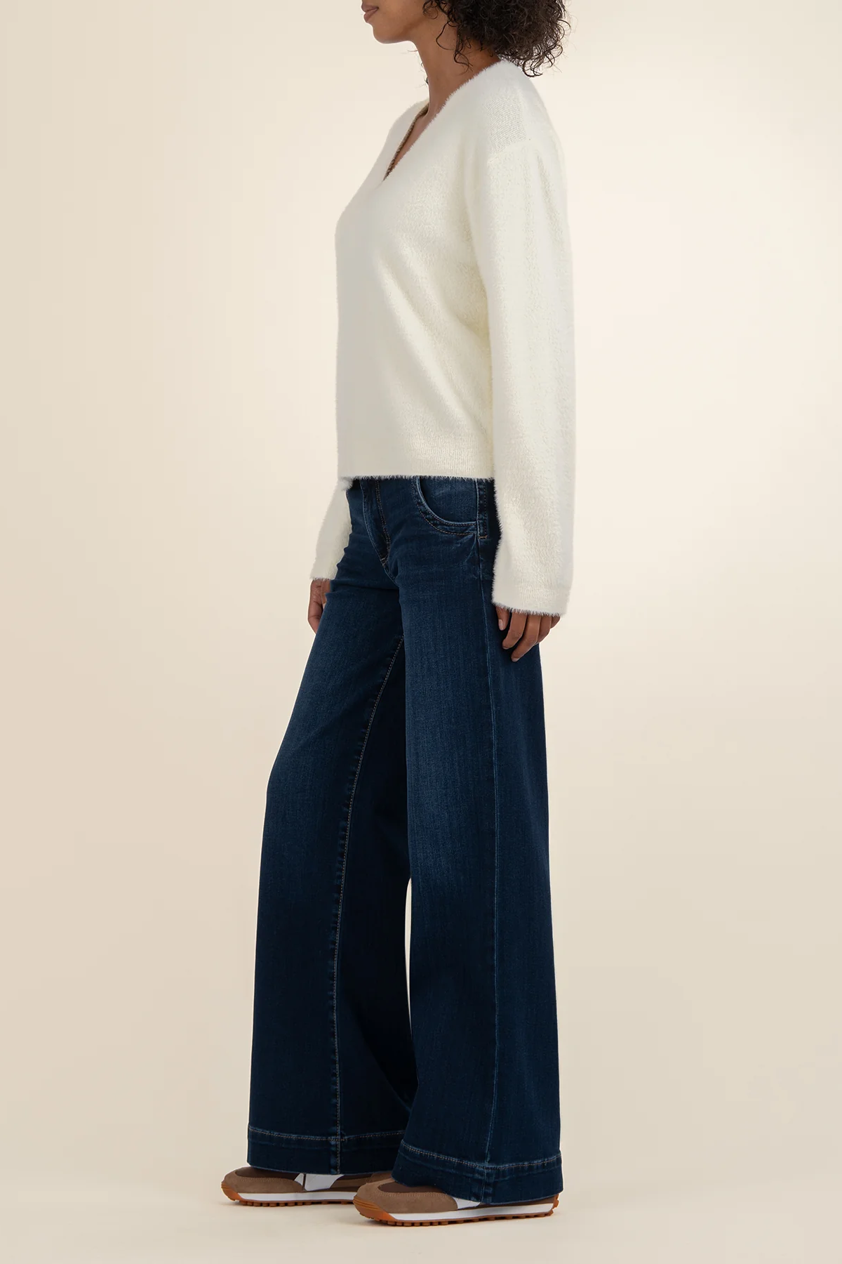 Person wearing a white sweater and dark blue jeans on a beige background