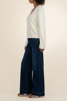 Person wearing a white sweater and dark blue jeans on a beige background