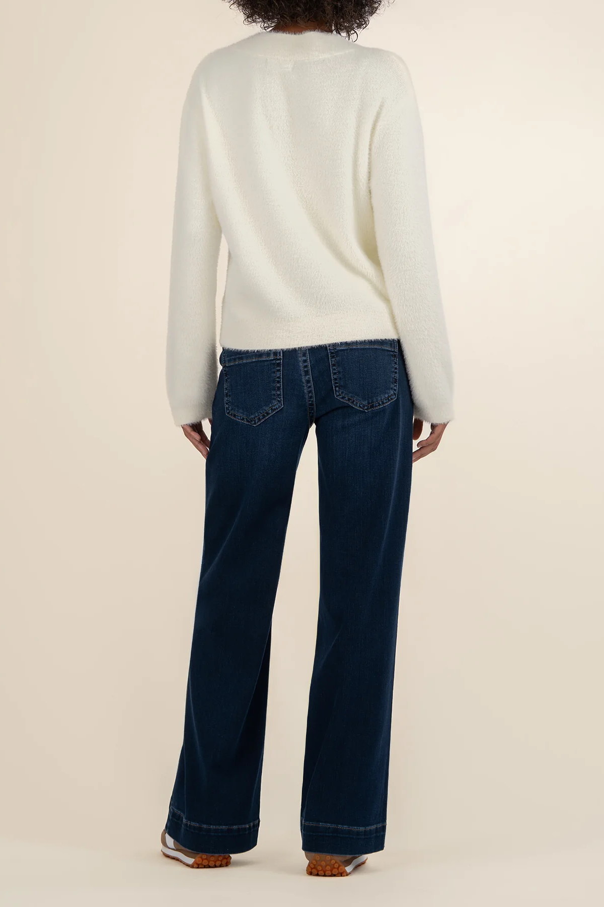 Person wearing a white sweater and dark blue jeans on a beige background