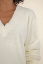 Close-up of a person wearing a white textured sweater against a neutral background