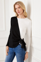 Woman wearing a black and white top with blue jeans against a white wall