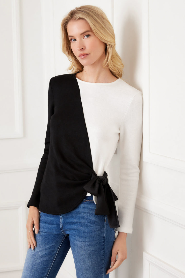 Woman wearing a black and white top with blue jeans against a white wall