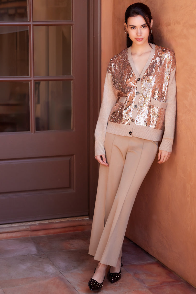 Woman wearing a sequined vest over a beige outfit against a warm-toned wall.