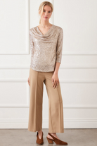 Woman wearing a beige sequin top and tan pants against a white background