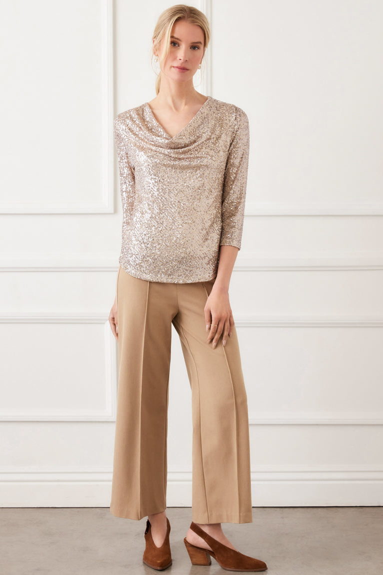 Woman wearing a beige sequin top and tan pants against a white background