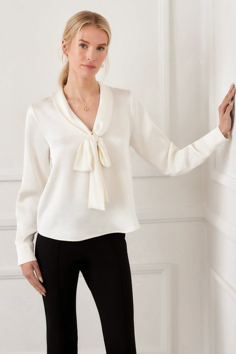 Woman wearing a white blouse with a bow tie against a white wall