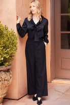 Woman in a black outfit standing outdoors against a beige wall.